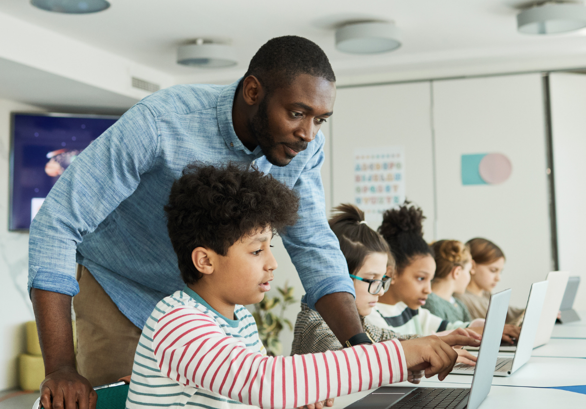 Teacher over students shoulder showing looking at something specific on a white laptop